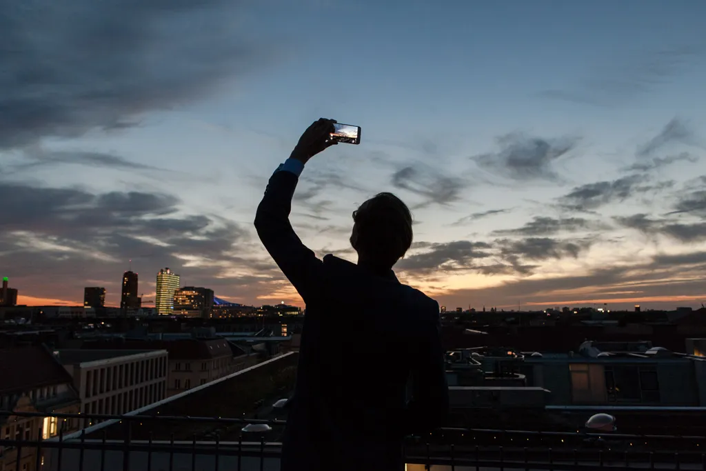 Die Silhouette eines Mannes von hinten, der einen Sonnenuntergang mit dem Smartphone fotografiert. Foto von William Veder · Eventfotografie Berlin | Eventfotograf aus Berlin.
